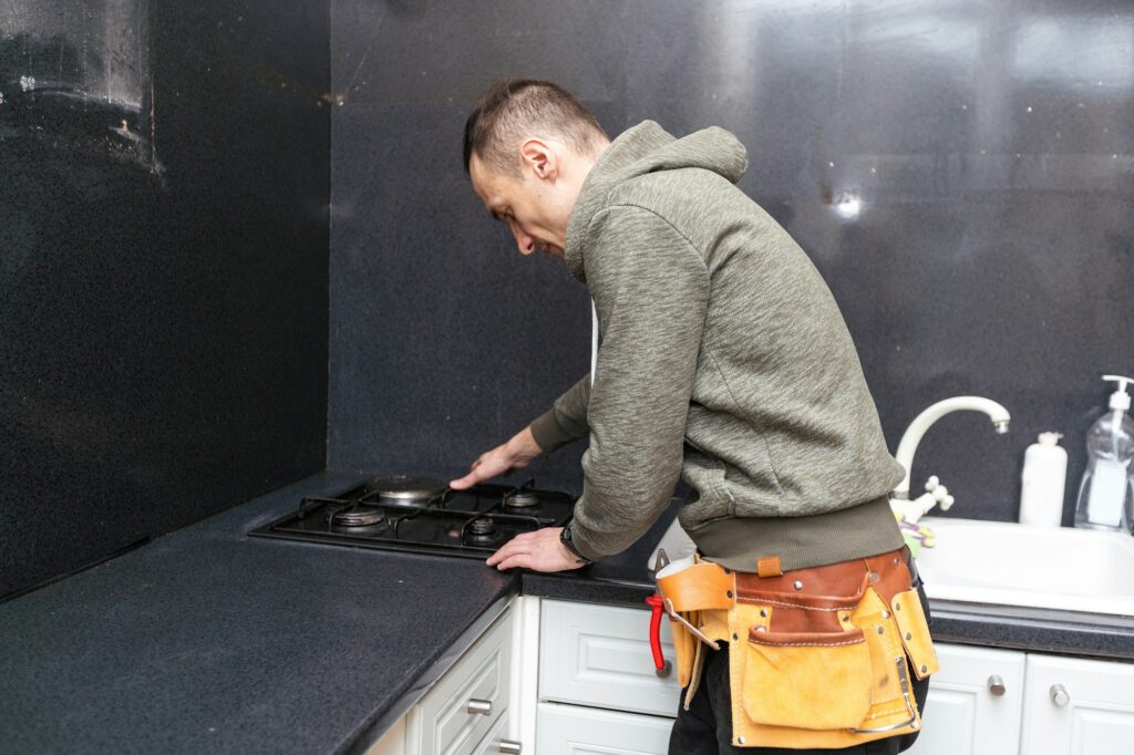 A gas engineer repairs a gas stove in the kitchen. The call of the master gas fitter to the house.