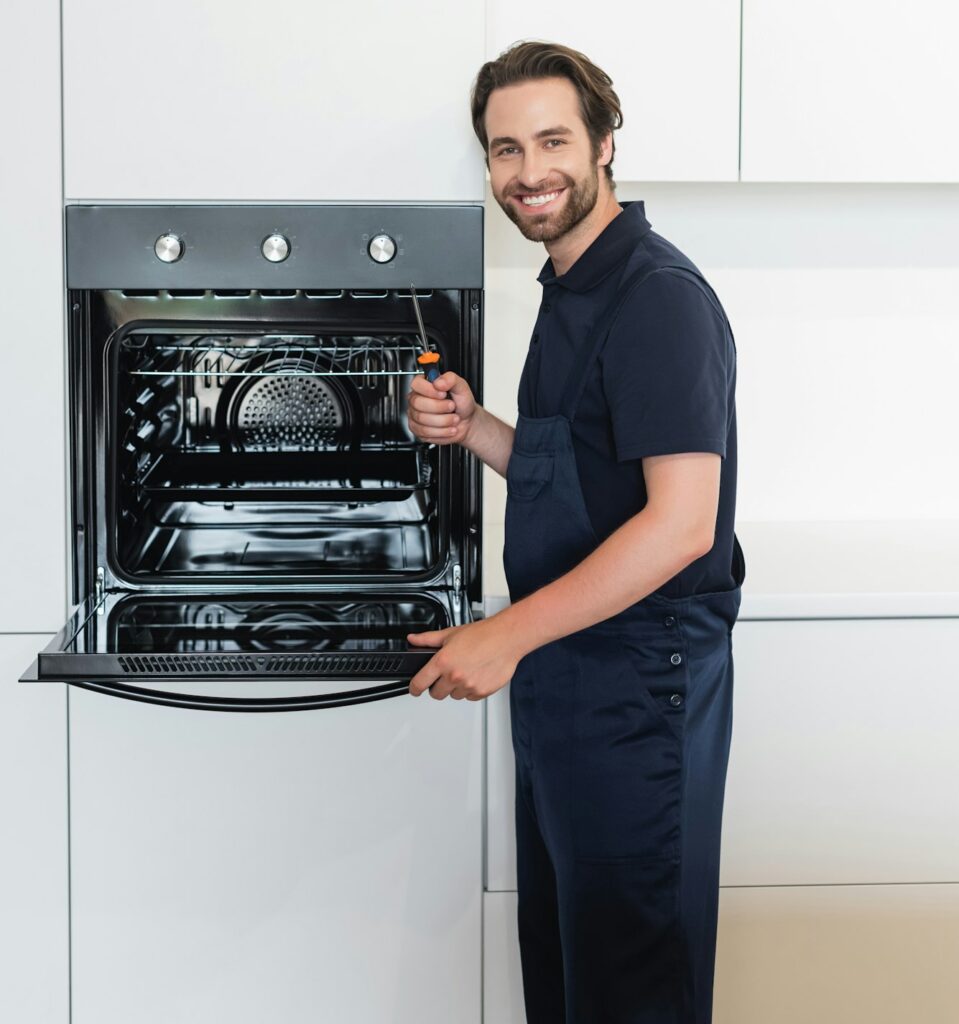 happy repairman with screwdriver smiling at camera near electric oven